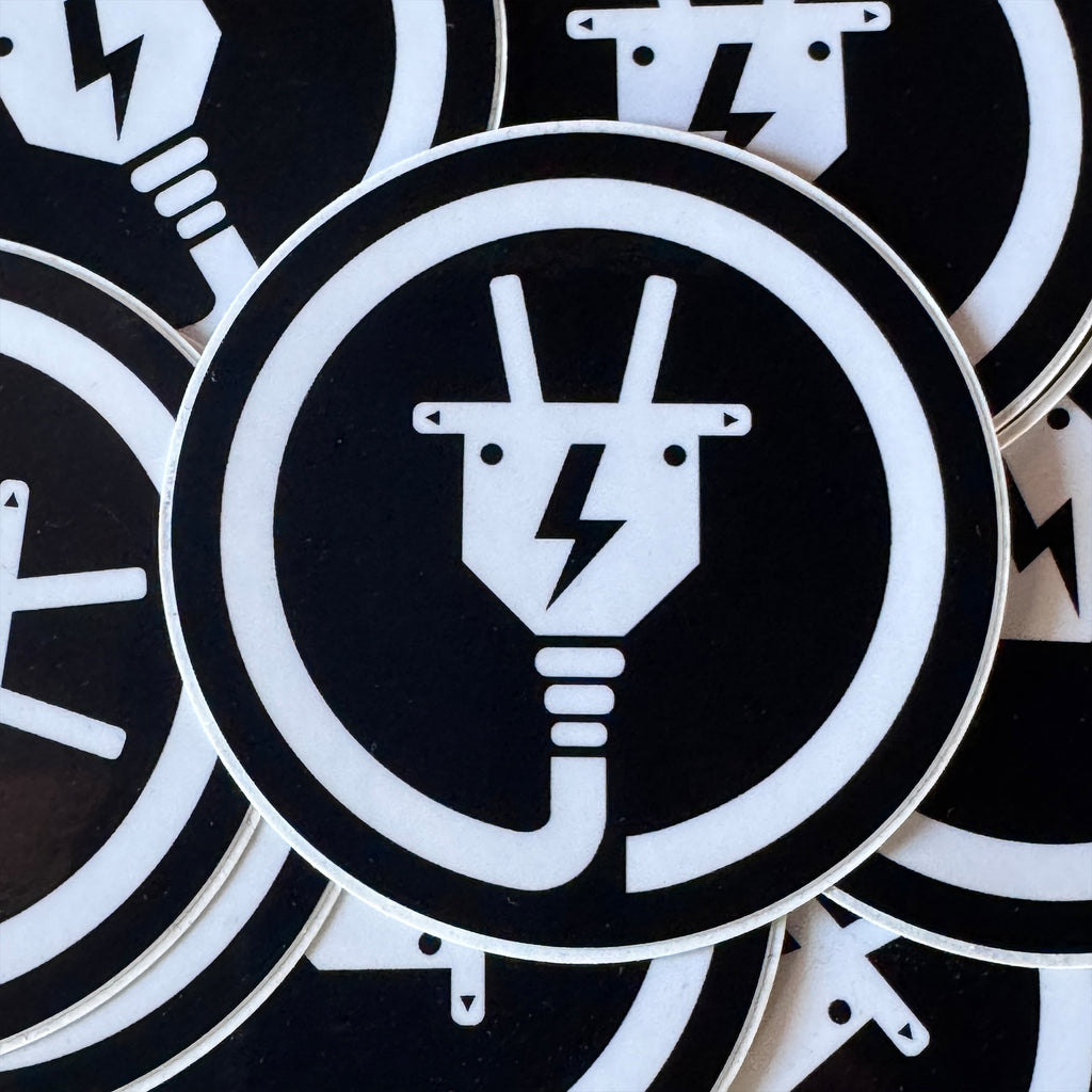 Circular black and white symbol from The Baby Goats with Electricity plug design on a black background.